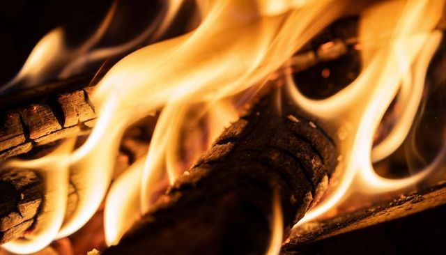 Crackling firewood flames wrapping charred logs with glowing embers and soot
