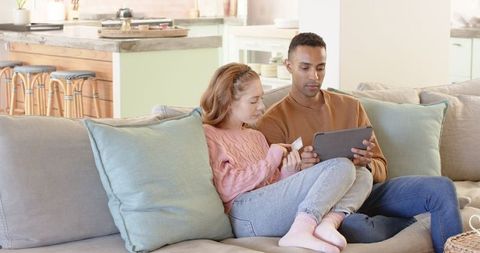 Diverse couple online shopping together on comfy couch at home