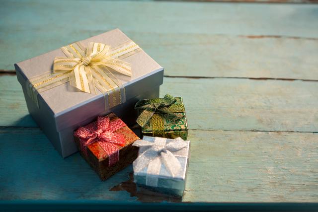 Colorful wrapped gifts with bows and ribbons placed on a rustic wooden plank. Ideal for holiday promotions, Christmas advertisements, festive greeting cards, and celebration-themed designs.