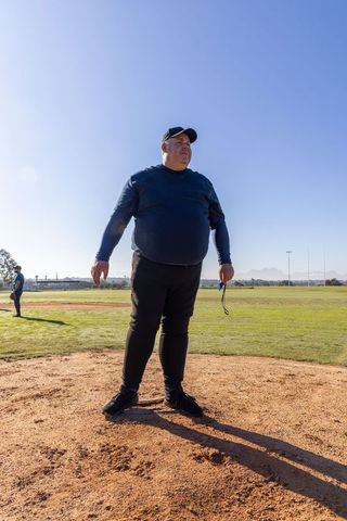 Senior baseball coach standing on pitcher's mound holding sunglasses on sunny field