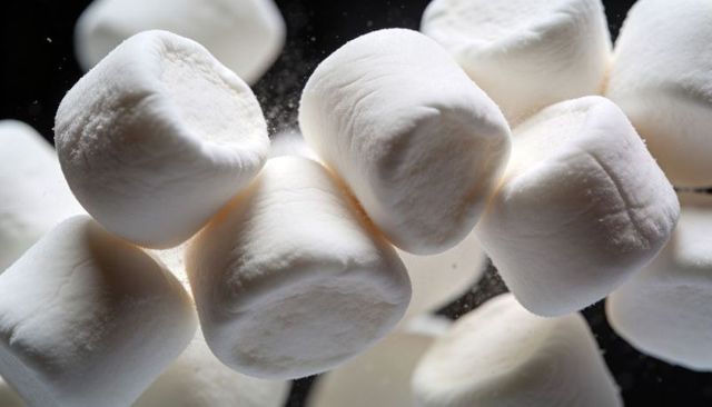 Floating white marshmallows dusted with sugar powder macro closeup on black matte background