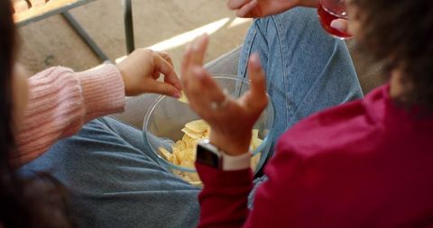 Friends sharing chips and drinks on sunny patio wearing jeans casual outdoor hangout