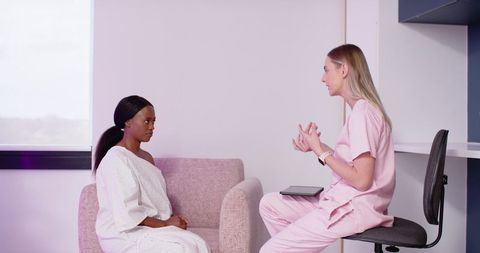 Clinician consulting patient on tablet in modern clinic wearing gown and pink scrubs