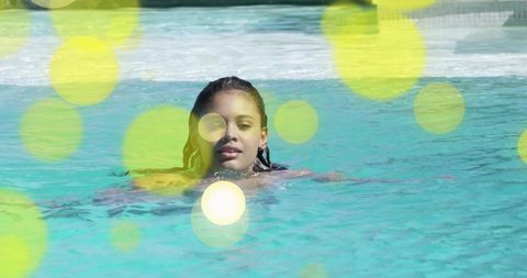 Teen swimming in turquoise pool with yellow-green bokeh and sunny lens flare