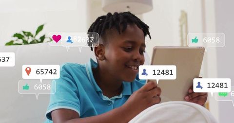 Smiling boy tapping tablet on sofa with floating social media notifications and icons