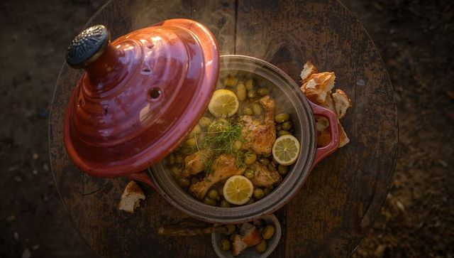Rustic moroccan chicken tagine with olives and lemon on weathered table at golden hour