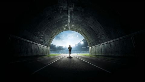Silhouette runner emerging from concrete tunnel into floodlit night stadium track arena