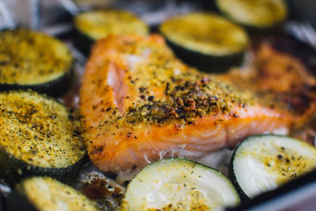 This image showcases a baked salmon fillet and zucchini slices generously sprinkled with herbs and seasonings. Suitable for illustrating articles and blog posts about healthy eating, easy dinner recipes, nutritious meal ideas, seafood dishes, or gourmet cooking tutorials.