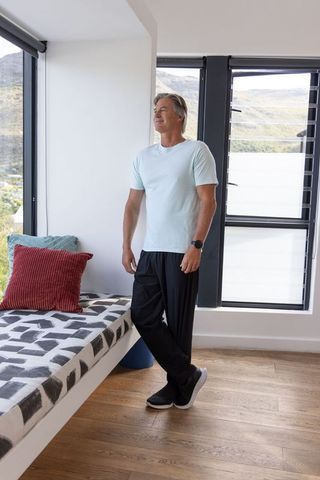 Mature man standing and looking out black-framed windows in modern bright home nook