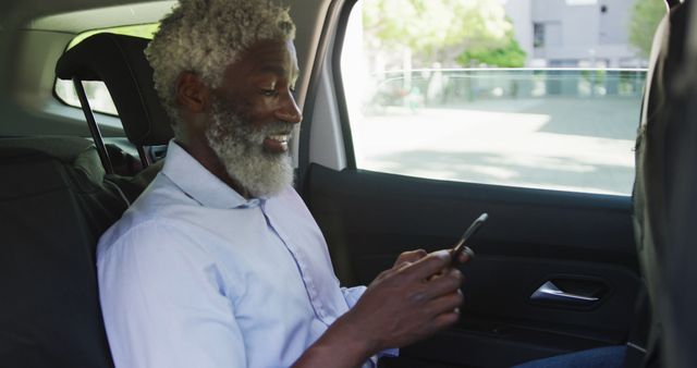 Senior man sitting in the backseat of car and using a smartphone, with a view of outside through window. Ideal for promoting technology use among older adults, advertisements featuring modern transport options, or content on seniors embracing technology during travel.