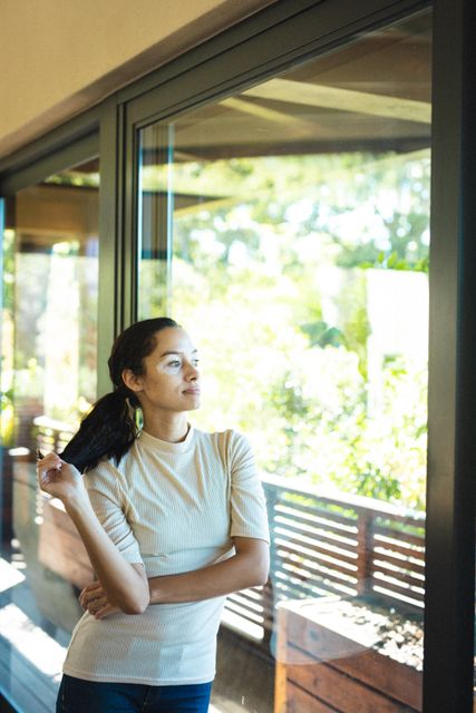Thoughtful biracial young woman looking away while leaning on glass window. unaltered, vitiligo, contemplation, lifestyle and leisure activity.