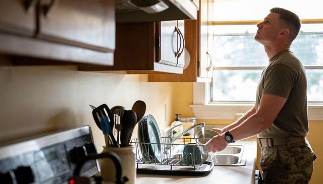 Soldier washing dishes in sunlit home kitchen showing military routine and discipline