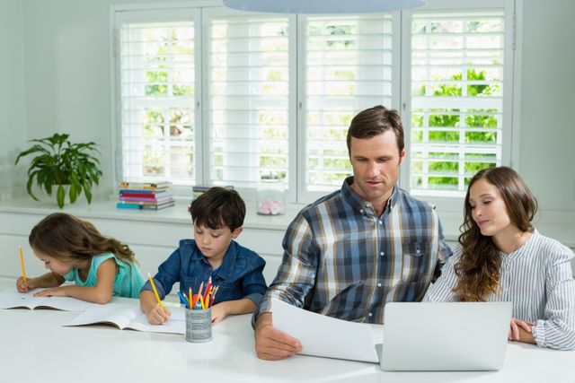 Parents working with laptop and childrens studying in living room at home