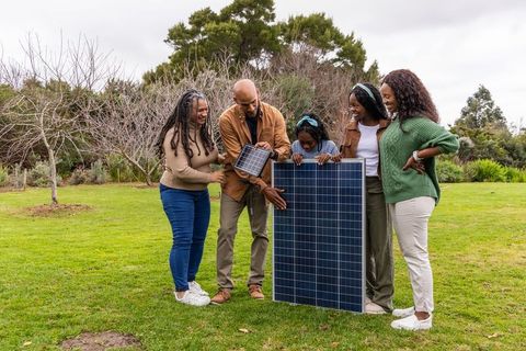 African american multigenerational family learning about solar panels on grassy lawn