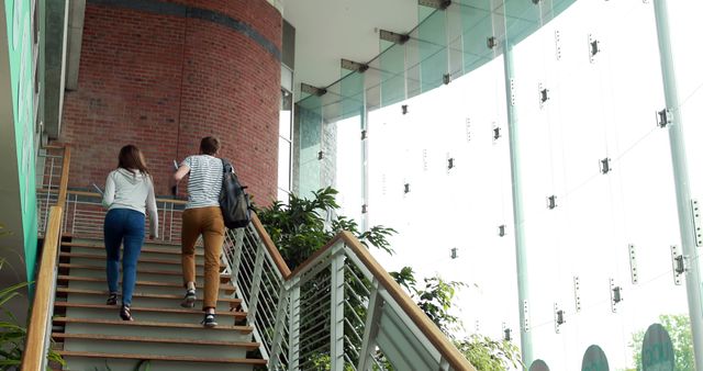 Two colleagues ascending office staircase with modern glass design - Download Free Stock Images Pikwizard.com