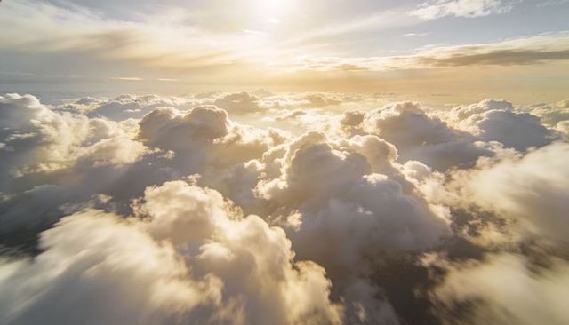 Glowing Sunrise Illuminating Towering Cumulus Clouds With Sun Shafts and Expansive Horizon