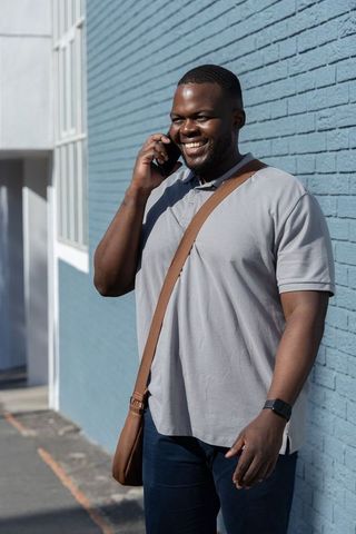 Smiling African American Man Walking and Talking on Smartphone by Blue Brick Wall