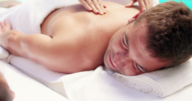 Man receiving relaxing back massage at a spa, promoting wellness and stress release. Ideal for use in advertisements for spa services, wellness blogs, and health magazines emphasizing relaxation and self-care.