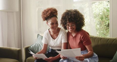 African American Friends Reviewing Documents Together on Sunlit Living Room Sofa