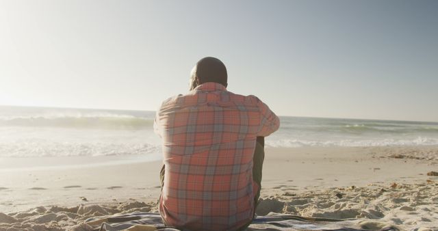 Man sitting on beach during sunset, relaxing and enjoying ocean view. Suitable for themes around vacations, relaxation, solitude and coastal living.