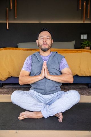 Mature asian man practicing seated meditation in cozy bedroom for mindfulness and calm