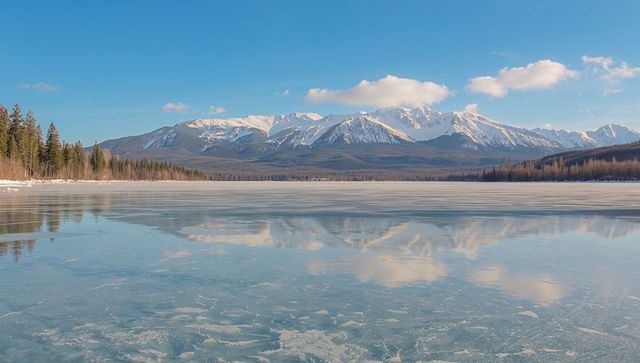 Sunlit snowcapped mountain range reflecting on glassy frozen lake with ice textures
