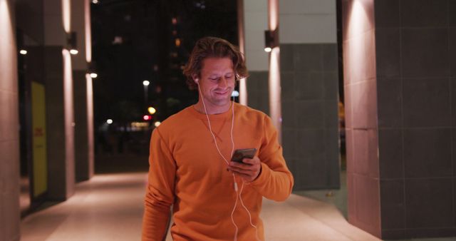 Man Wearing Orange Sweater Walking Outdoors with Earphones at Night - Download Free Stock Images Pikwizard.com
