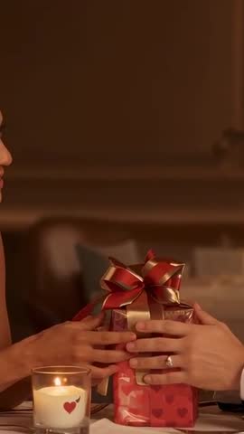 Couple Exchanging Gift at Candlelit Dinner Reaching Hands Showing Ring
