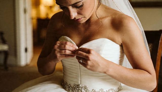 Bride adjusting strapless wedding gown with beaded belt and veil, intimate bridal prep