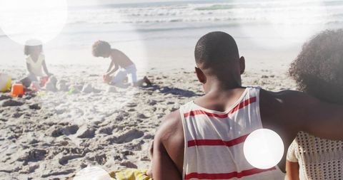 Family relaxing on sunlit beach while children building sandcastles together