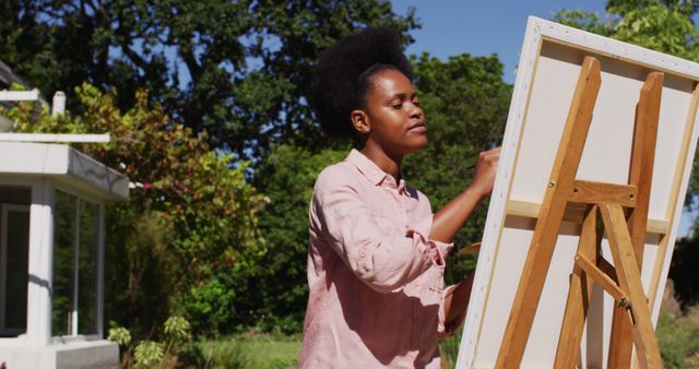 African american woman painting picture on canvas in sunny garden. staying at home in isolation during quarantine lockdown.
