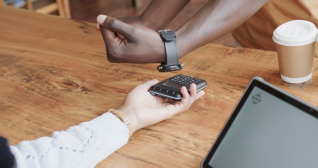 Capturing a moment where an individual pays for a purchase using a smartwatch's contactless payment feature in a cafe. This technology-driven approach showcases the convenience and growing trend of digital wallets. Can be used in articles about mobile technology, financial innovations, or contemporary consumer behavior. Ideal for websites, blogs, advertisements, and marketing materials focusing on modern lifestyle, technological advancements, or financial technology.