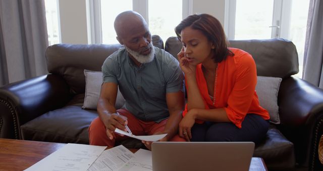 Front view of mature black couple sitting on the couch and discussing bills in a comfortable home. Woman talking on mobile phone 4k