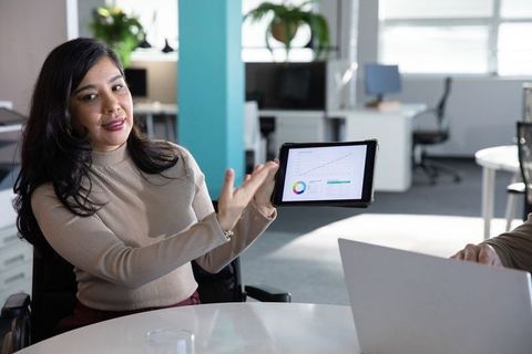 Indian businesswoman presenting tablet with growth chart to diverse team in modern office