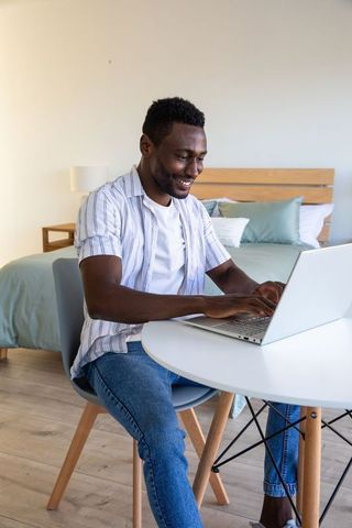 African American Man Working on Laptop in Minimalist Bedroom Setting