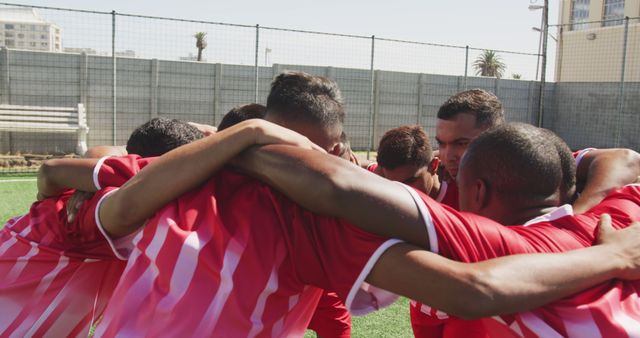 Team of male soccer players wearing red jerseys huddling on outdoor field, demonstrating teamwork and unity. Useful for sports-related topics, team building exercises, competitive spirit, and promotional materials for soccer events or trainings.
