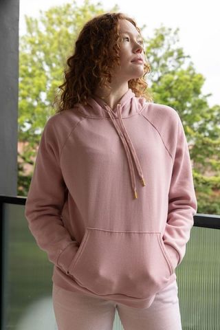 Pensive redhead woman standing on balcony in pastel pink hoodie looking upward