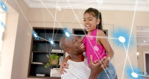 Smiling father lifting daughter at home sharing joyful family bond with digital connection