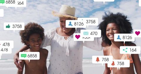 Smiling grandmother hugging grandchildren on sunny beach with social media bubbles