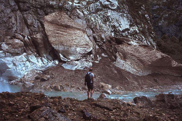 Man hiking near mountain stream, standing among rocky terrain. Ideal for nature, travel blogs, adventure magazine covers, promoting outdoor gear and fitness advertisements.