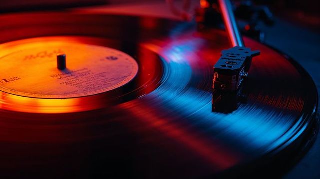 Spinning vinyl record turntable with tonearm stylus and neon reflections