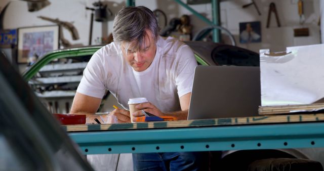 Mechanic Working at Desk in Garage with Laptop and Coffee - Download Free Stock Images Pikwizard.com