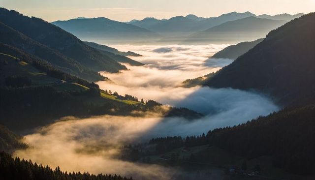 Sunlit morning fog filling alpine valley with mist and rolling pastures