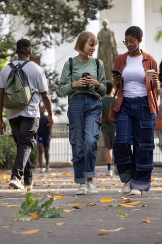 Diverse college friends walking on campus holding coffee, backpacks and smartphone