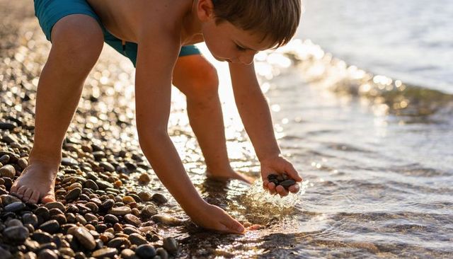Boy collecting pebbles on pebbled shore at golden hour, barefoot child playing by lake