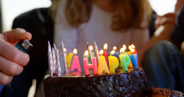A close-up of a birthday cake with colorful letters spelling 'HAPPY' and lit candles. A person is lighting the candles, ready for celebration. Ideal for birthday party invitations, celebration themes, and festive content.