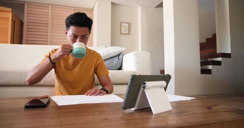 Man Drinking Coffee While Working On Tablet At Home