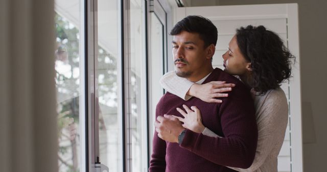 Romantic hispanic couple embracing cuddling standing in window. at home in isolation during quarantine lockdown