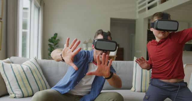 Father and son wearing VR headsets engaging with virtual reality in a modern living room. This scene embodies family bonding through immersive technology, showing a modern parenting approach involving interactive entertainment. Ideal for use in advertisements for VR technology, family activities, modern living, or technology in education and family bonding contexts.