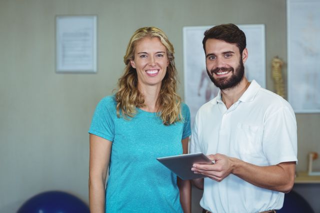 Physiotherapist and patient standing together in clinic, both smiling and holding a digital tablet. Ideal for use in healthcare, medical, and wellness contexts, showcasing professional consultation, therapy sessions, and patient care.